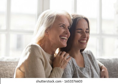 Overjoyed senior mother or granny hugging happy grown up adult daughter or grandchild, looking aside, watching TV, laughing, having fun, enjoy spending free time together head shot close up portrait. - Shutterstock ID 1653376603