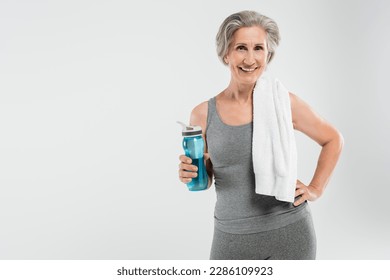 overjoyed senior woman with white towel on shoulder holding sports bottle with water isolated on grey - Powered by Shutterstock