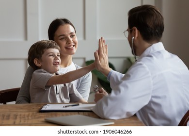 Overjoyed small boy patient with young mom visit male doctor greeting at consultation in hospital. Happy little kid give high five make deal with pediatrician in clinic. Children healthcare concept.