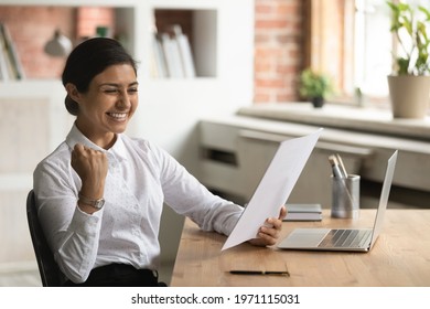 Overjoyed Smiling Indian Businesswoman Reading Good News In Letter, Sitting At Work Desk, Excited Young Woman Received Scholarship, Job Promotion Or Offer, Showing Yes Gesture, Celebrating Success