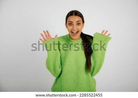 Overjoyed woman in light green monochrome pullover with raised hands. Female studio portrait, white background. Young woman with big smile posing in oversized casual wear. Fashion, stylish clothes.