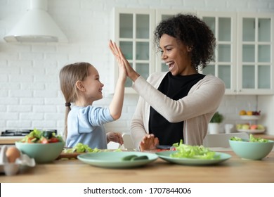 Overjoyed young African American mom and little Caucasian daughter give high five cooking at home together, smiling biracial mother and small girl child have fun preparing healthy food in kitchen - Powered by Shutterstock