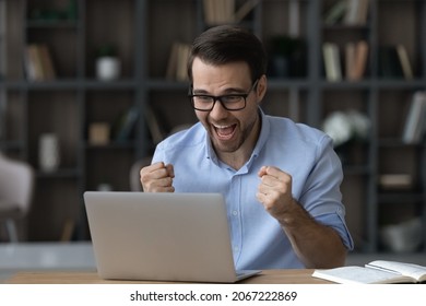 Overjoyed young businessman manager in glasses celebrating online lottery auction betting win, making successful profitable deal, feeling excited looking at computer screen in modern home office room.