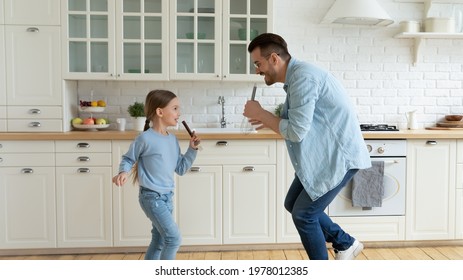 Overjoyed young Caucasian father have fun sing in kitchen appliances with small daughter. Happy dad play and dance at home with little teen girl child on leisure family weekend. Parenthood concept. - Powered by Shutterstock