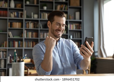 Overjoyed young caucasian man looking at smartphone screen, getting online lottery win notification or reading email with unbelievable good news, feeling motivated and joyful at modern office.