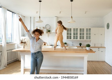 Overjoyed Young Caucasian Mother And Little 8s Daughter Have Fun Dancing Together In New Renovated Kitchen. Happy Mom And Small Girl Child Celebrate Moving Relocation To Own Home. Rent Concept.