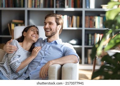 Overjoyed Young Couple Having Fun, Laughing At Funny Joke At Home. Emotional Family Spouses Cuddling Relaxing On Sofa, Enjoying Spending Weekend Free Leisure Time, Communicating Together Indoors.