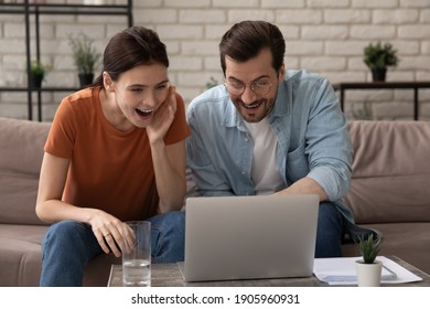 Overjoyed young couple looking at laptop screen, sitting on couch at home, happy surprised man wearing glasses and woman excited by good news reading in email, get unexpected notification, online win