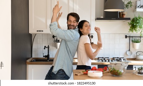 Overjoyed Young Couple Renters Have Fun In Kitchen Celebrating Moving To New Home Together. Happy Millennial Man And Woman Tenants Dance Near Counter Cooking Healthy Food. Relocation Concept.