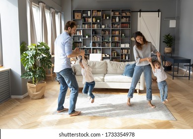 Overjoyed Young Family With Little Preschooler Daughters Have Fun Playing Together In Living Room, Happy Caucasian Parents Dance Swirl Engaged In Funny Activity With Small Girls Children At Home