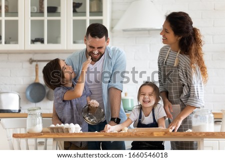Overjoyed young family with little preschooler kids have fun cooking baking pastry or pie at home together, happy smiling parents enjoy weekend play with small children doing bakery cooking in kitchen