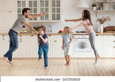 Overjoyed Young Family With Small Kids Entertain In Modern Spacious Kitchen Dancing Together, Happy Playful Parents Have Fun With Little Preschooler Children Engaged In Funny Activity At Home