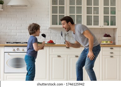 Overjoyed Young Father Entertain Sing And Dance Using Kitchen Appliances With Cute Little Preschoolers Son, Happy Funny Dad Have Fun Play With Small Boy Child, Enjoy Family Weekend At Home