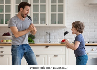 Overjoyed Young Father And Little Preschooler Son Have Fun Singing Together Using Kitchen Appliances, Happy Playful Dad Parent Play With Smiling Excited Small Boy Child Entertain At Home