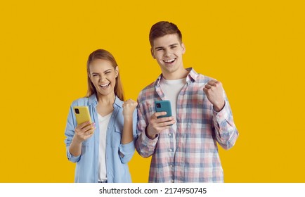 Overjoyed Young Friends Caucasian Man And Woman Experience Positive Emotions When They See Notification On Mobile Phone About Great Shopping Offer Dressed In Casual Clothes, Stand In Yellow Studio