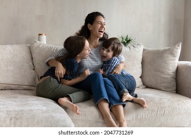 Overjoyed young hispanic mother cuddling small laughing kids siblings, having fun entertaining resting together on comfortable sofa. Joyful multigenerational family playing on weekend at home. - Shutterstock ID 2047731269
