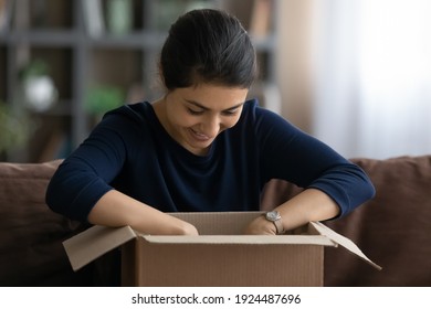 Overjoyed young Indian woman open unpack cardboard box with internet order shopping online from home. Excited millennial ethnic female buyer unbox package buying on web. Delivery service concept.