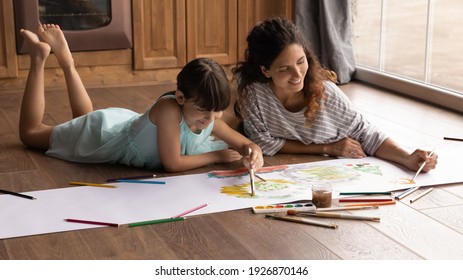 Overjoyed Young Latino Mother And Small 8s Daughter Lying On Floor At Home Have Fun Painting Together With Colors. Happy Hispanic Mom Or Nanny And Little Girl Child Enjoy Drawing. Hobby Concept.