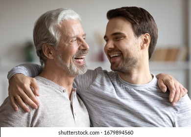 Overjoyed young millennial man embrace mature dad have fun talk and laugh at home, happy elderly father hug grown-up adult son enjoy family weekend reunion, show family love and care