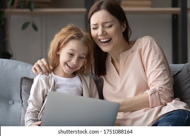 Overjoyed Young Mom Or Nanny Relax On Sofa With Little Girl Child Laugh Watching Funny Video On Laptop, Happy Mother And Small Daughter Have Fun Browsing Internet Using Modern Computer At Home