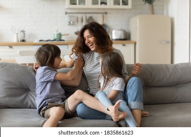Overjoyed young mother having fun with two kids at home, laughing happy mum, adorable little daughter and son playing funny active game, tickling, sitting on cozy couch in living room - Shutterstock ID 1835861623