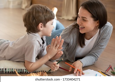 Overjoyed young mother   small preschooler son give high five playing drawing together  happy mom nanny have fun painting paper learning and little boy child at home  education concept