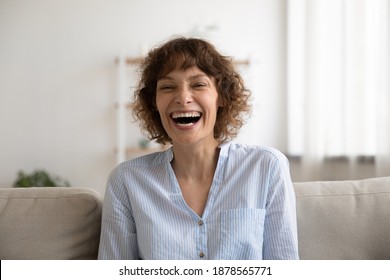 Overjoyed Young Pretty Female Laughing On Cute Funny Joke Demonstrating Perfect Straight White Teeth. Joyful Millennial Woman Sit On Couch At Living Room Look At Camera Can Not Keep Sincere Laughter