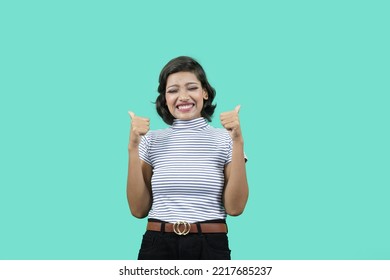 Overjoyed Young Pretty Woman, Eyes Closed, Screamed, Smiling Joyfully And Looking Happy Showing Thumbs Up With Both Hands, Feeling Carefree And Positive With Both Thumbs Up Against Blue Wall.