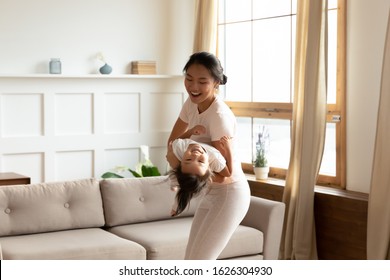 Overjoyed Young Vietnamese Mother Have Fun Enjoy Weekend With Cute Little Biracial Daughter At Home, Happy Asian Mom Or Nanny Play With Small Girl Child In Living Room Involved In Activity Together