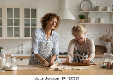 Overjoyed Young Woman And Elderly 60s Mother Have Fun Laugh Cooking Tasty Food Together At Home. Smiling Adult Grownup Daughter And Mature Mom Enjoy Family Weekend Baking Pies Cookies In Kitchen.