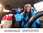 Overjoyed young woman in Santa Hat driving car with Xmas gift boxes nearby and enjoy music, singing song feeling enjoyment of winter holiday preparation