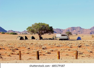 Overland Offroad Safari Truck And Group Of Tents At Campsite Under Acacia Tree (Camel Thorn), Outdoor Camp In Namib Naukluft Desert, Sossusvlei (Sossus Vlei), Namibia, Africa