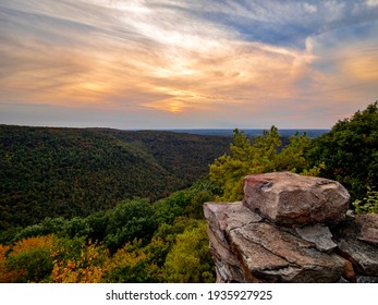 Overlook of the mountains and the fall foliage at Coopers Rock State Forest in West Virginia with the sunset golden sky one direction and a blue swirly sky the other direction, with the rock cliff.
