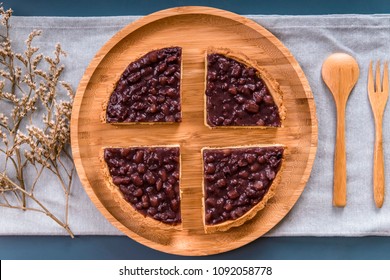 Overlook The Red Bean Pies,the Wooden Fork,the Wooden Spoon And Dried Flowers On The Round Wooden Plate With 
Plain Cloth And Navy Blue Background