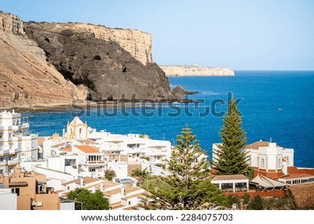 Overlooking Luz Bay from the viewpoint in May provides a tranquil rugged scene with a panoramic view of black cliff Rocha Negra and coastline, while the rooftops of Luz village below offer a contrast.