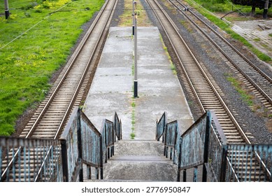 Overlooking an old train station platform with two parallel sets of rusty railway tracks, offering a view of a long, potentially challenging journey and the concept of reaching a destination
