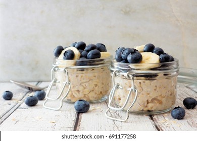 Overnight oats with fresh blueberries and bananas in jars on a rustic white wood background - Powered by Shutterstock