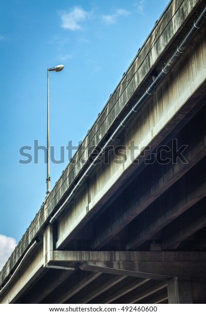 An overpass bridge light standard from below\
against a blue sky background. highway bridge. street lamp with\
blue sky. Street light on the bridge on blue sky background.\
Flyover. Bridge and lamp.