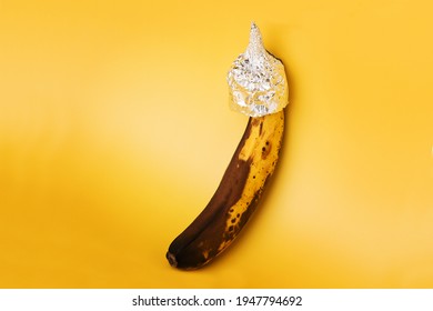 Overripe Banana In Aluminium Foil Hat On Yellow Background.