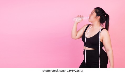 Oversize Weight Loss Concept. Chubby Overweight Fat Young Woman With Measuring Tapes Drinking Fresh Water From Bottle In Her Hands After Workout While Standing Over Isolated Pink Background.