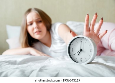 Overslept Young Woman Awake In Pajamas Turns Off Alarm Clock In Hurry. Morning Routine And Wake Up Late From Alarm Clock In Bed. Woman Is Late In Panic After Sleeplessness Insomnia. Unhealthy Sleep