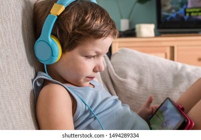 Overstimulated Children Concept. Too Much Screen Time. 4 Years Boy In Headphones Watching Videos While Tv Is Working. 