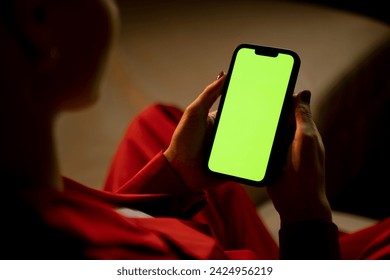 An over-the-shoulder view captures a woman using a smartphone with a green screen, potentially browsing or awaiting interaction. - Powered by Shutterstock