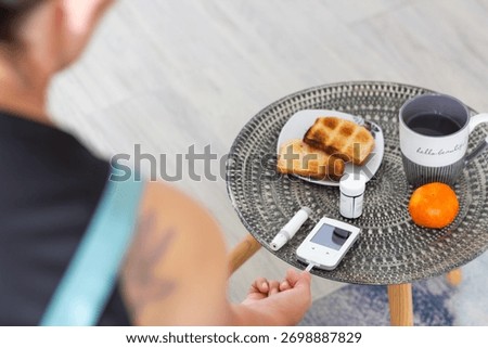 Over-the-shoulder view of a glucometer and lancing device next to a healthy meal (toast, tangerine, tea). Represents diabetes management, healthy eating, and routine health checks.