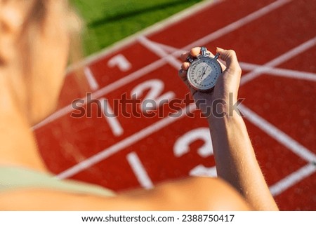 Over-the-shoulder view of a person holding a stopwatch at a running track