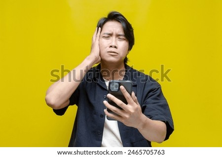 an overthinker young Asian man in pensive mood holding phone with sad and thoughtful expression. Asian man holding phone while questioning and wondering.