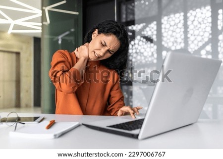 Overtired business woman working inside office with laptop, Hispanic female worker has severe neck pain, massaging muscles with hand