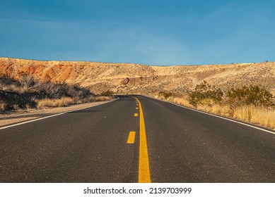 Overton, Nevada, USA - December 11, 2010: Valley Of Fire. Ground Level Shot Over Black Asphalt Road With Yellow Divider Line Cuts Through Brown Desert Hills Under Blue Sky.