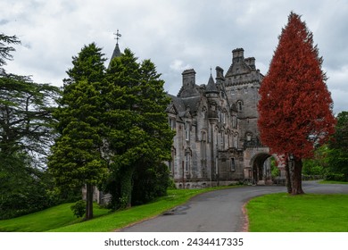Overtoun House in Scotland stands majestic amidst lush greenery and red tree. Charming historic country house with stunning Victorian architecture and stone facade surrounded with beautiful garden. - Powered by Shutterstock
