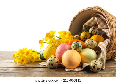 Overturned basket with painted Easter eggs and flowers on table against white background